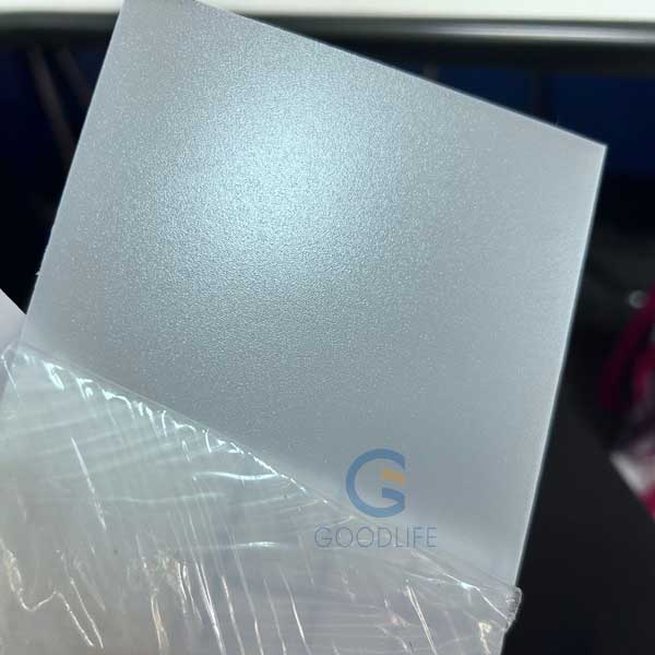 Gros plan main tenant un panneau diffuseur de polycarbonate dépoli mettant en valeur la texture mate et les propriétés de diffusion lumineuse